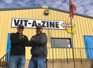 Two men standing in front of a building with the words vit-a-zine on it.
